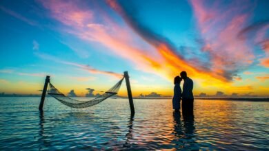 A romantic couple shares a kiss at sunset with vibrant skies over the Maldives beach.