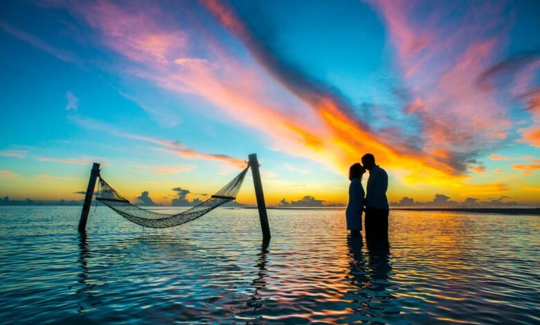 A romantic couple shares a kiss at sunset with vibrant skies over the Maldives beach.