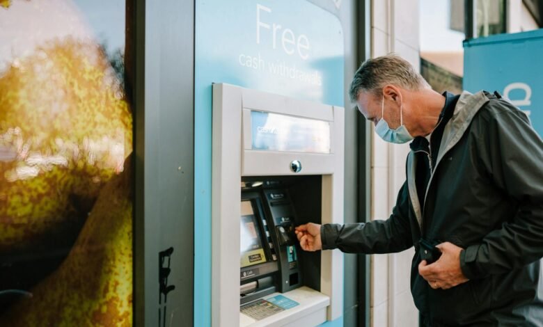 A man wearing a mask using an ATM machine outdoors for cash withdrawal.