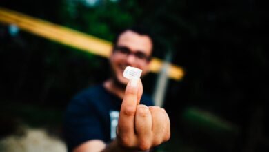 Selective Focus Photo of Man in Black T-shirt Hand Glasses Holding Out Piece of Paper