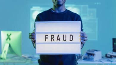 A man holding a sign reading 'FRAUD' in a tech environment, highlighting cybersecurity concerns.