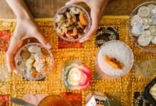 Hands arranging traditional Persian snacks for Nowruz on a decorated table with candlelight.