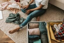 Woman organizing clothes while sitting on floor with open suitcase, preparing for a trip.