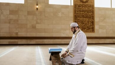 Man kneeling in prayer inside a mosque, wearing traditional Islamic clothing.