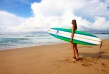 woman standing near sea holding white, blue, and green surfboard under blue sky