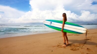 woman standing near sea holding white, blue, and green surfboard under blue sky