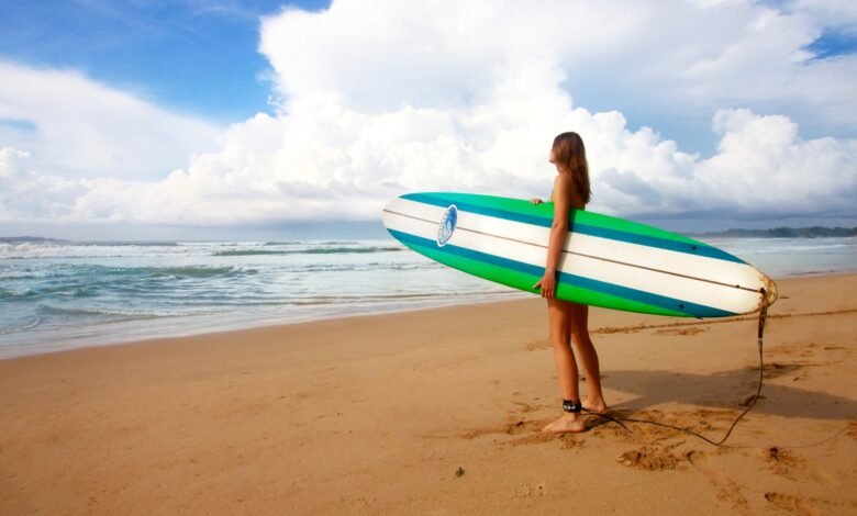 woman standing near sea holding white, blue, and green surfboard under blue sky