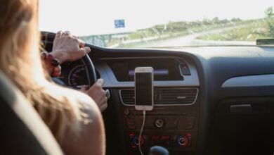 View from behind a woman driving a car on a sunny day with a phone mounted on the dashboard.