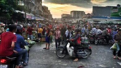 Vibrant street scene in Phnom Penh market filled with people and motorbikes, capturing local life.