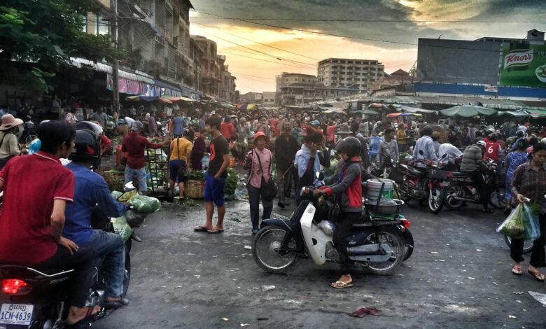 Vibrant street scene in Phnom Penh market filled with people and motorbikes, capturing local life.