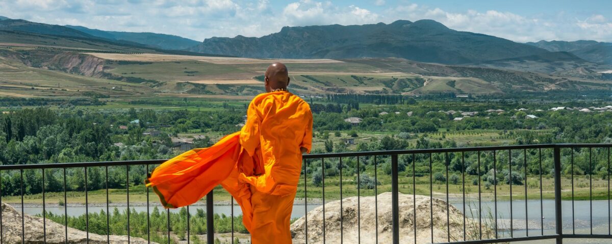 man in orange robe standing on gray concrete floor during daytime