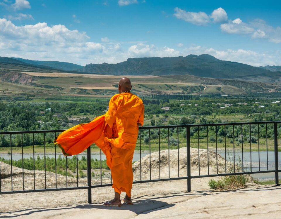 man in orange robe standing on gray concrete floor during daytime