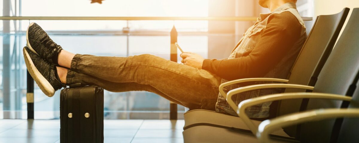 man sitting on gang chair with feet on luggage looking at airplane